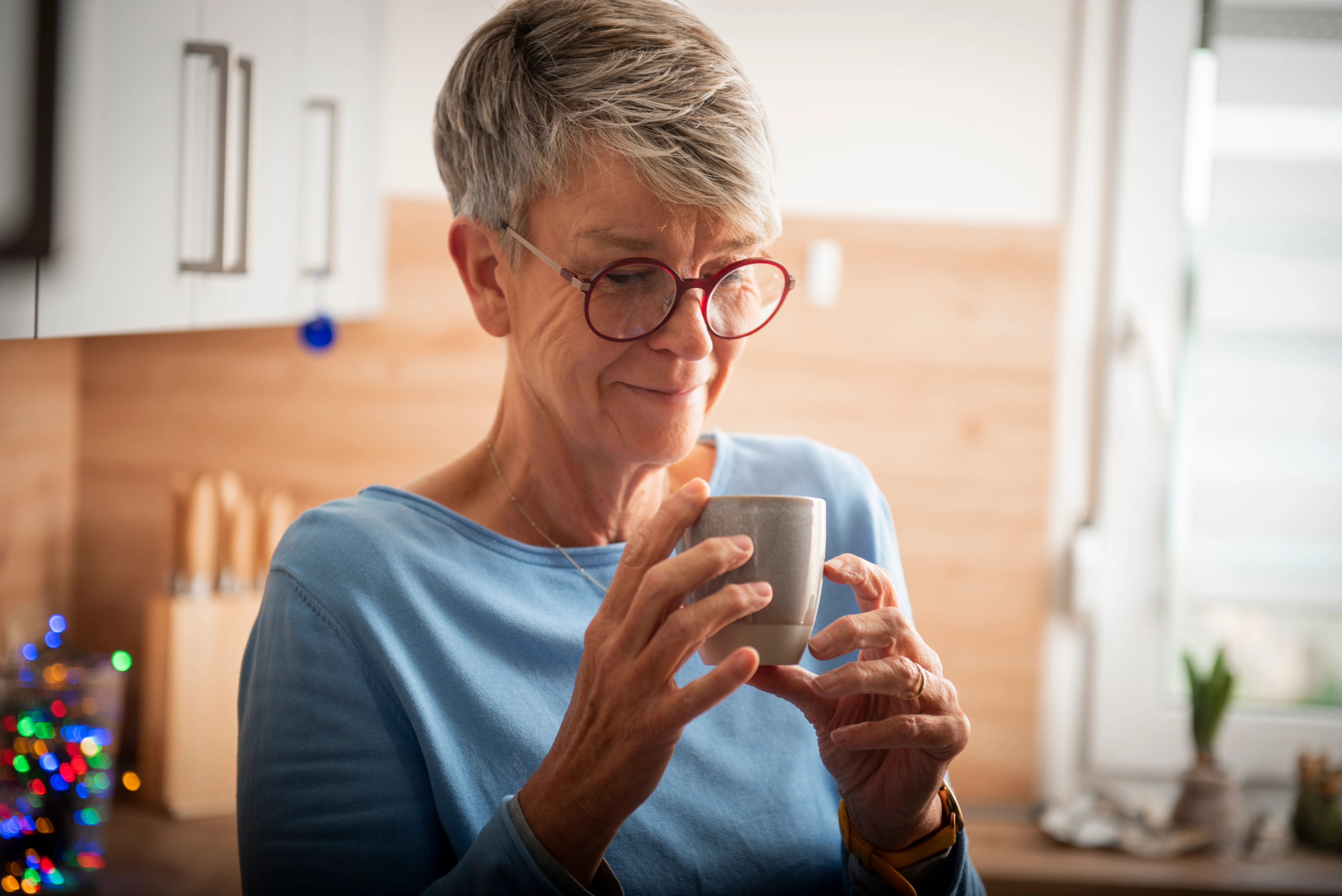 Frau sitzt friedlich mit einer Tasse Tee am Fenster